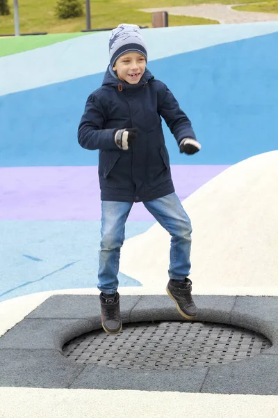 穿着保暖衣服的男孩跳上了现代游乐场的蹦床 — 图库照片