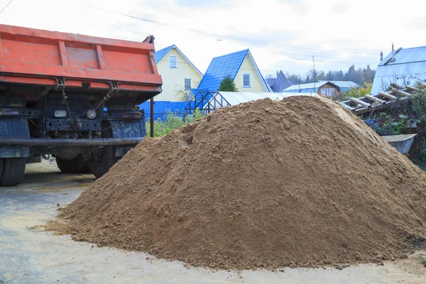 pile of sand on ground in foreground and dump truck in background on construction site