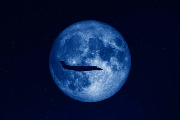 Silhouette of private jet plane flying against huge full moon in dark starry space toned in trendy Classic Blue color of the Year 2020. Elements of this image furnished by NASA