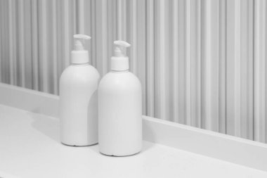 Gri banyoda çizgili duvarlı bir rafta iki beyaz şişe.