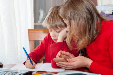 Uzaktan öğrenme, evde uzaktan eğitim. Sosyal uzaklık nedeniyle uzaktan eğitim alan annenin yardımıyla evden ders çalışan bir çocuk. Anne oğluna ev ödevinde yardım ediyor ya da Covid-19 salgını sırasında evden e-öğreniyor. 