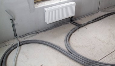 Yeni bir apartman dairesinde elektrik kabloları ve ısıtma boruları döşenmiş radyatör.