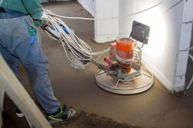 Sanatçı, yeni apartmanın inşaat alanında kum ve çimento döşeme işi yapıyor ve cilalıyor. Kum ve beton zemin perdelendi