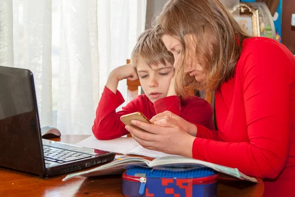 Child studying from home with help of mother taking remote class because of social distance. Mother helping her son with his homework or e-learning from home during Covid-19 pandemic lockdown