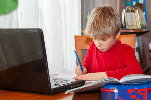 School kid in self isolation using laptop for homework, Social Distance learning online education during coronavirus epidemic. Cute boy studies and does school homework at home during quarantine