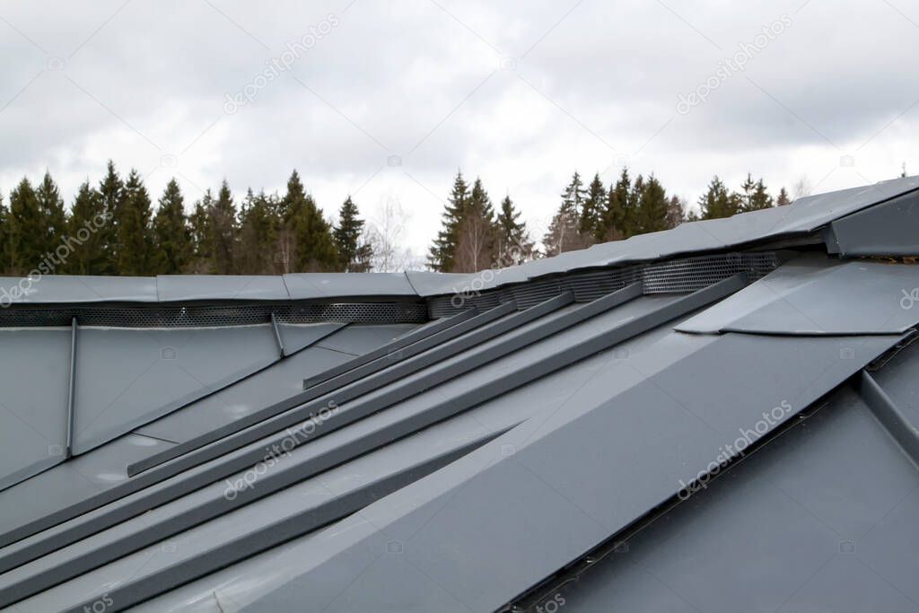 close-up view of an independent black metal folding roof and ventilation grilles with trees and sky behind