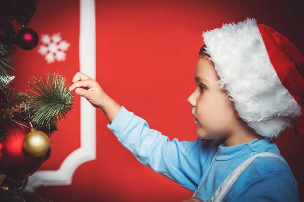 Beautiful portrait of little boy in Santa hat decorating the Christmas tree new year room. The idea for postcards