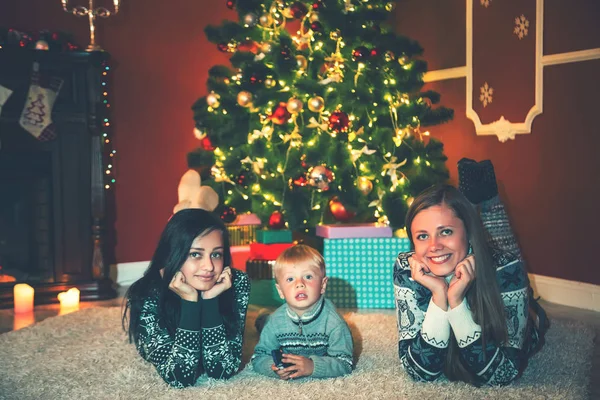 Joven familia y niño cerca de un árbol de Navidad en la habitación decorada con regalos . — Foto de Stock