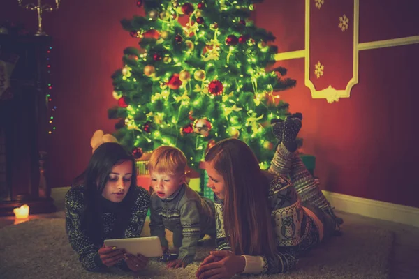 Mladá rodina a dítě poblíž vánoční strom ve vyzdobeném pokoji četl knihu. — Stock fotografie