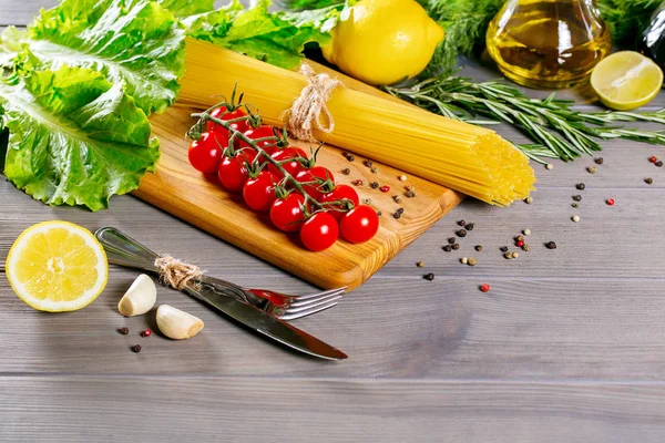 Spaghetti crudi, erbe aromatiche e spezie con coltello e forchetta su fondo grigio antico — Foto Stock