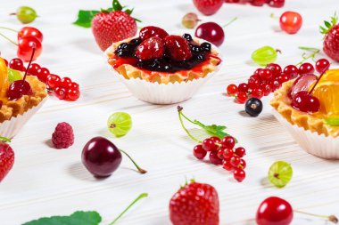 Lezzetli meyve kek çilek, kiraz, kuş üzümü ve ahududu ile beyaz ahşap zemin üzerinde. Güzel, keyifli ve sağlıklı tatlılar