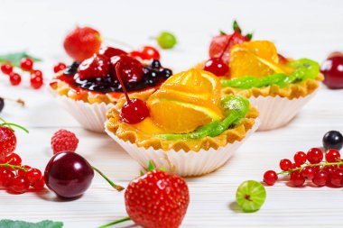 Lezzetli meyve kek çilek, kiraz, kuş üzümü ve ahududu ile beyaz ahşap zemin üzerinde. Güzel, keyifli ve sağlıklı tatlılar