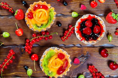 Lezzetli meyve kek çilek, kiraz, kuş üzümü ve ahududu kahverengi ahşap zemin üzerine. Güzel, keyifli ve sağlıklı tatlılar