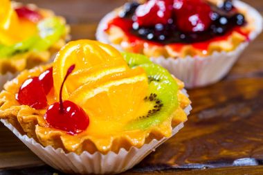 Lezzetli meyve kek çilek, kiraz, kuş üzümü ve ahududu kahverengi ahşap zemin üzerine. Güzel, keyifli ve sağlıklı tatlılar