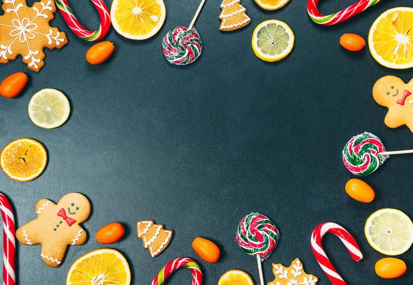 Christmas background with sweets, candy and gingerbread with oranges, lemons and mandarins on a vintage black background. New Year\'s frame with free space