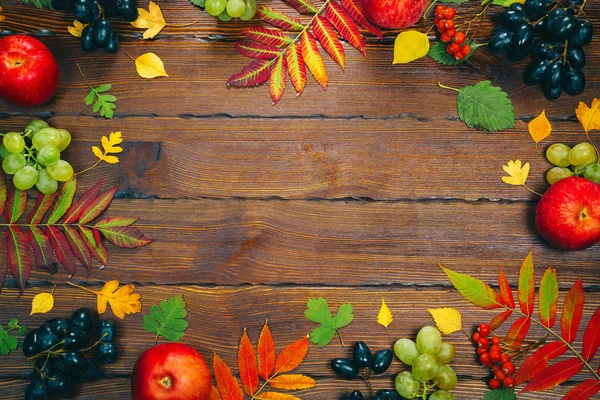 Mooie kleurrijke herfst bladeren, bessen, appels en druiven frame op houten achtergrond met vrije ruimte. Herfst festival — Stockfoto