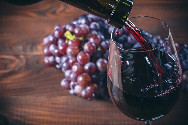 Despejando Vinho Tinto Copo Com Monte Uvas Vermelhas Contra Fundo — Fotografia de Stock