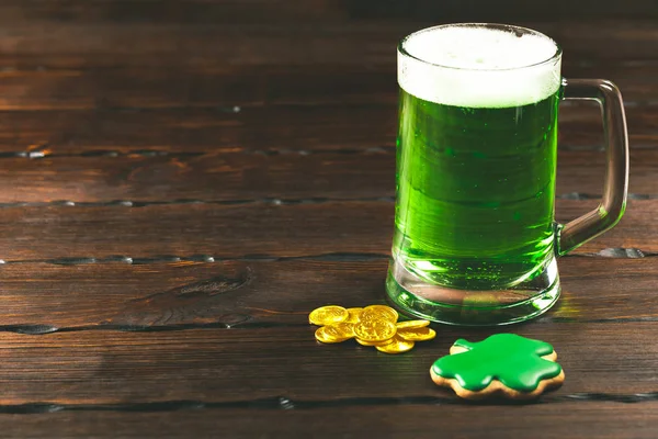 帕特里克节背景与一杯绿色啤酒和三叶草姜饼与金币的木质背景 — 图库照片