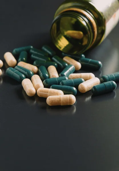 Closeup of medical capsules or pills of drug. A lot of two-color pills spill out of bottle on black background. Vintage color tone — Stock Photo, Image