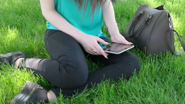 Female student with tablet PC sitting on grass in campus park — Stock Video