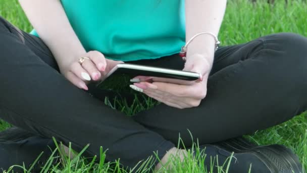 Junge Frauen sitzen mit gekreuzten Beinen im Gras und arbeiten Tablet-PC uhd — Stockvideo