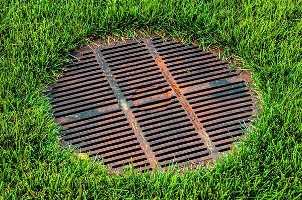 Gridded sewer manhole on green lawn — Stock Image Gridded sewer manhole on green lawn Royalty Free Stock Images