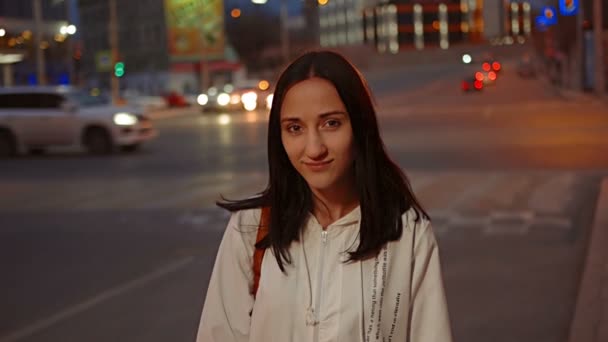 Счастливая девушка позирует на улице перед размытым городским движением ночью — стоковое видео
