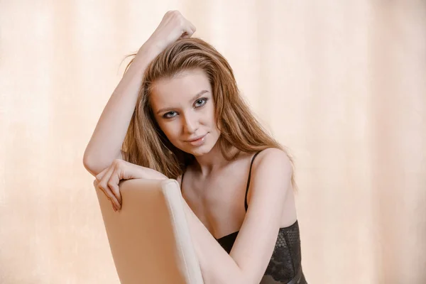 Jonge vrouw in lingerie poseren op stoel in de kamer met copyspace op warme kleur van de gordijnen toned — Stockfoto