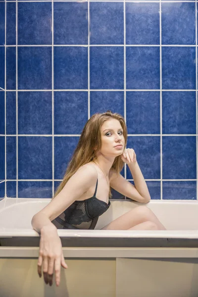 Junge Frau beim Baden. Badezimmer Zeit. Seitenansicht von sexy Frau in Spitzenunterwäsche sitzt in einem Bad vor gefliester Wand von blauer Farbe gefärbtes Bild. — Stockfoto