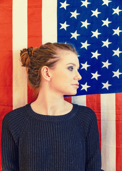 Young gender fluid person looking away in front of US stars and stripes flag vintage color.