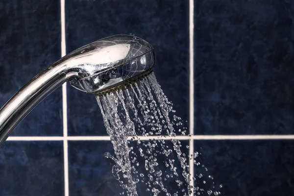 Pomme de douche sur fond carrelé avec flux de gouttes d'eau s'envolant, copyspace — Photo