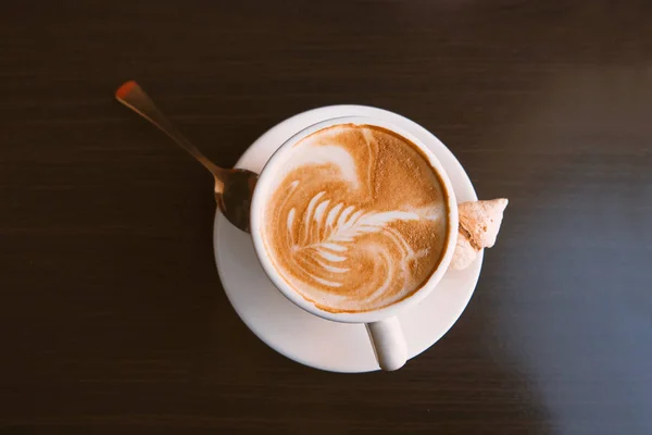 Top view of a mug of latte coffee with art on foam on dark wood background. — Stock Photo, Image