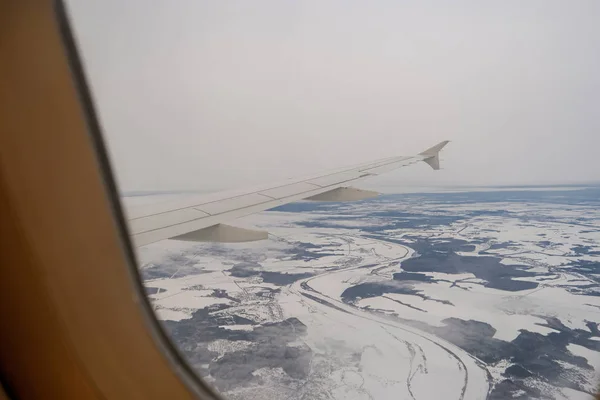 带着雪在陆地上空飞行。客机翼和冬季景观之下. — 图库照片