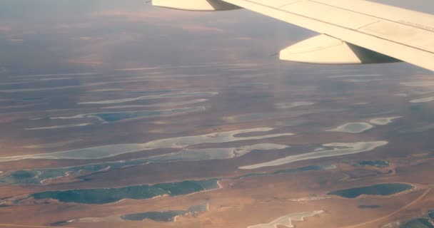 Крыло самолета, летящего над землей с озерами. Вид из окна самолета — стоковое видео