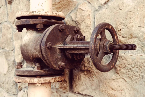 Válvula de agua antigua sobre un fondo de una pared de piedra natural. Válvula grande y oxidada en el primer plano del tubo de agua —  Fotos de Stock