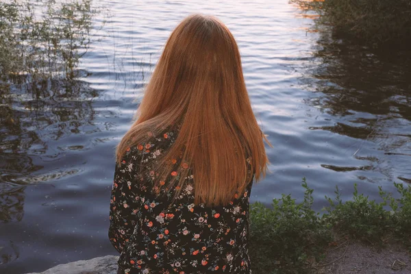 Donna dai capelli rossi rilassante guardando il tempo del tramonto sull'acqua del fiume — Foto Stock