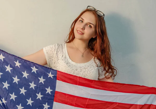 Junge Frau mit amerikanischer Flagge in den Händen, die auf ein farbiges Vintage-Bild blickt — Stockfoto