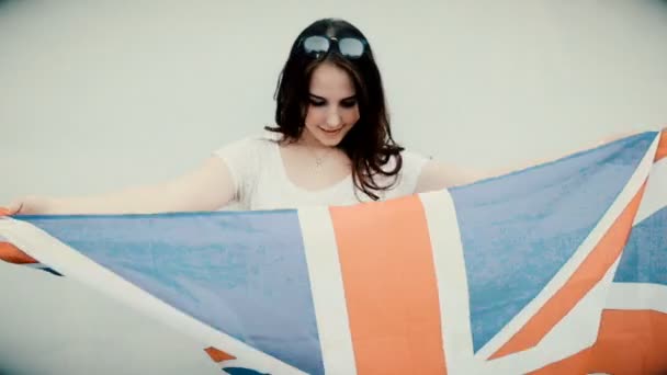 Giovane donna latina tiene Union Jack bandiera davanti al suo corpo con orgoglio e gioia, vintage cercando granuloso vecchio filmato — Video Stock