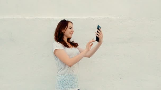 Side view of a young woman with a tablet computer in front of white wall — Stock Video