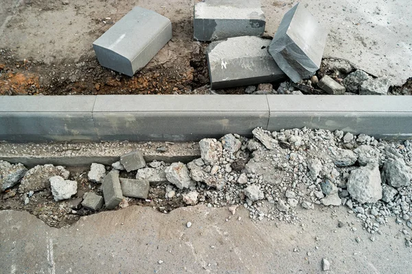 Curdstones lying on the sidewalk near the pit for installing a border. Broken asphalt surface on the side. A hole in the road surface. Repair of road work — Stock Photo, Image
