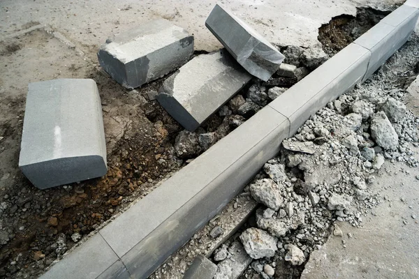 Ремонт асфальтового бордюра. Куча поворотных камней, лежащих на тротуаре возле ямы для установки границы . — стоковое фото