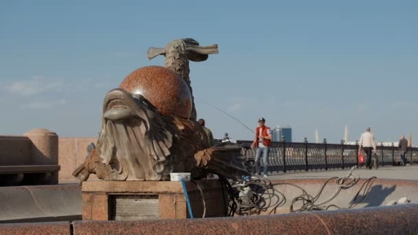 Astrakhan, russland, 24. april 2018: sommerliche szene: Fisch-Drachen-Brunnen in instandhaltung mit perl auf dem rücken und wolga-fluss-damm mit menschen und sensen im hintergrund — Stockvideo