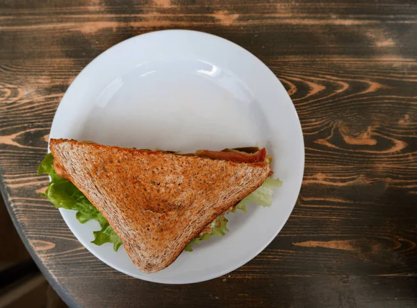 Τόστ σάντουιτς με ζαμπόν, τυρί και λαχανικά στο πιάτο στο ξύλινο τραπέζι — Φωτογραφία Αρχείου