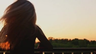 Sarışın kız gün batımında nehir kenarında uzun beyaz saçlarını sallıyor.