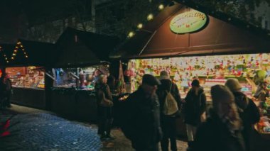 Bonn Almanya, 23 Aralık 2019: Kalabalık Noel pazarının aydınlatılmış tezgahları boyunca yürüyor 4k ağır çekim