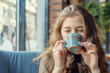 Kızıl saçlı kız bir fincan çaydan içer.