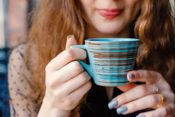 A curly girl with red hair poses in a cafe holding a Japanese-style cup at her juicy lips — Stock Photo, Image