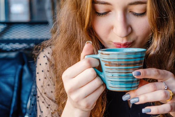 Het meisje drinkt een warm drankje uit een keramische beker met haar dicht bij haar lippen. — Stockfoto