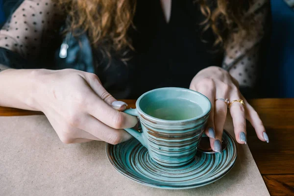 De meisjes handen houden een kopje thee vast. Het meisje poseert in een café. beeld in donkere tinten. — Stockfoto