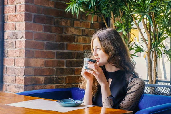 Το κορίτσι κάθεται στο καφέ στο τραπέζι και κρατάει ένα φλιτζάνι ζεστό ποτό.. — Φωτογραφία Αρχείου